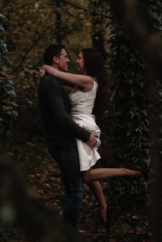 Man lifting woman whilst they smile at eachother, she has one leg kicked out and her arms wrapped around his neck