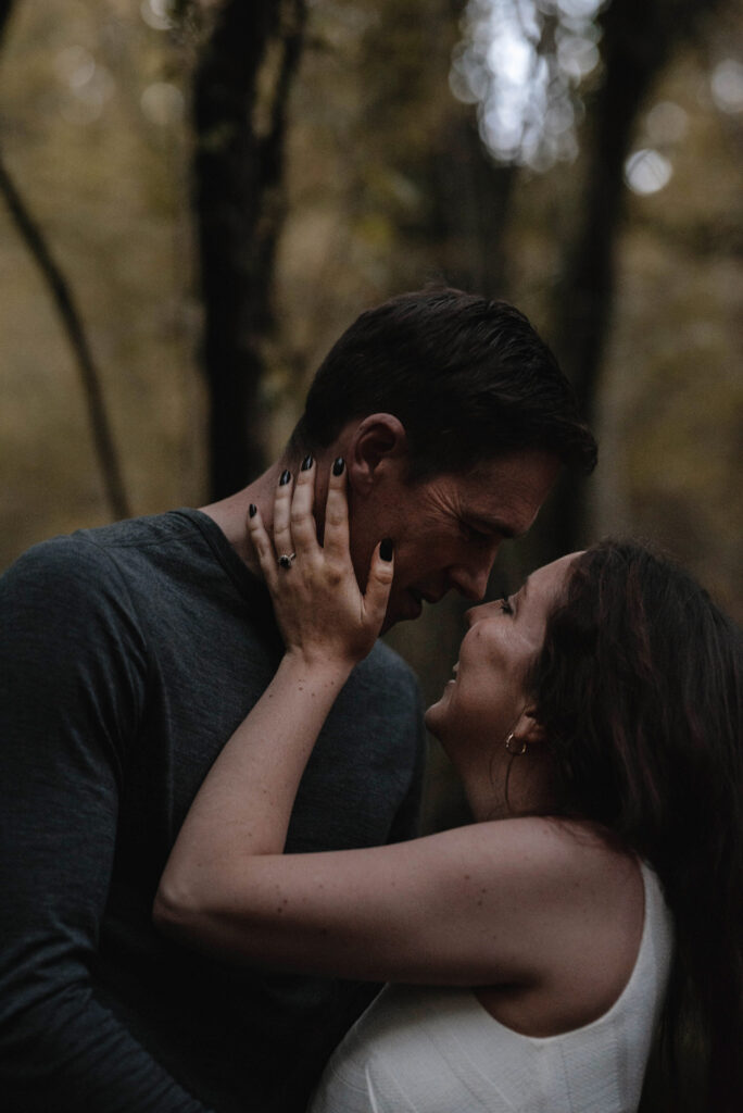 Woman looking up at man and smiling whilst she touches his face, an engagement ring is on her finger
