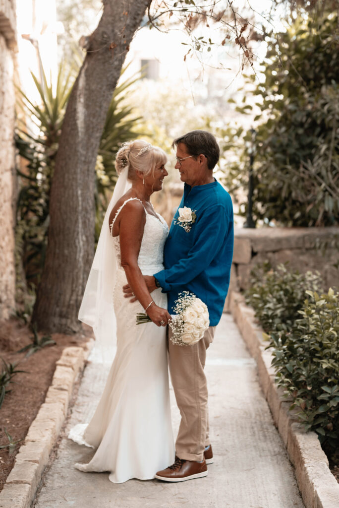 Bride and Groom facing each other and smiling in a private garden, the bride is holding her bouquet in front of them. 