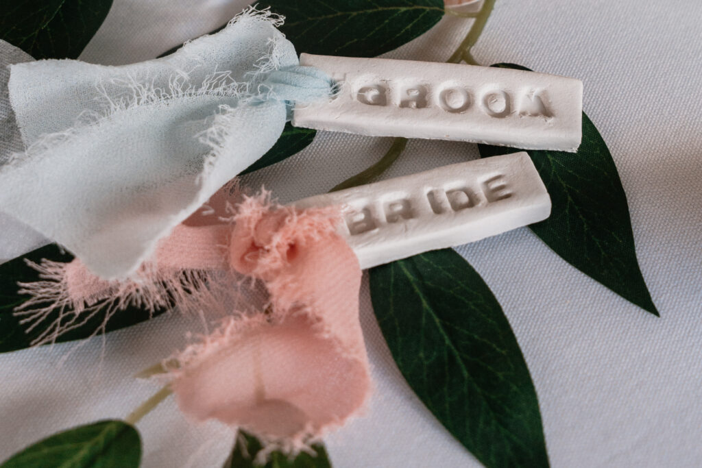 Bride and Groom clay placenames with coloured ribbons lay on top of a white tablecloth