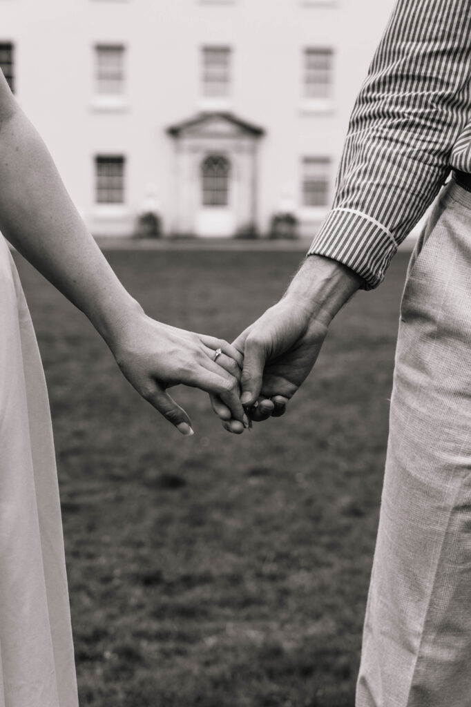 A close up of a man and woman holding hands, showing her engagement ring