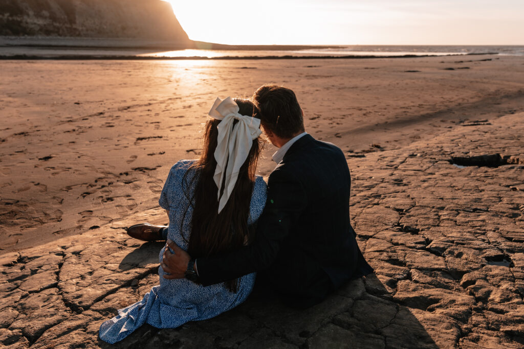 A man and woman sat on the beach looking at the sunset 