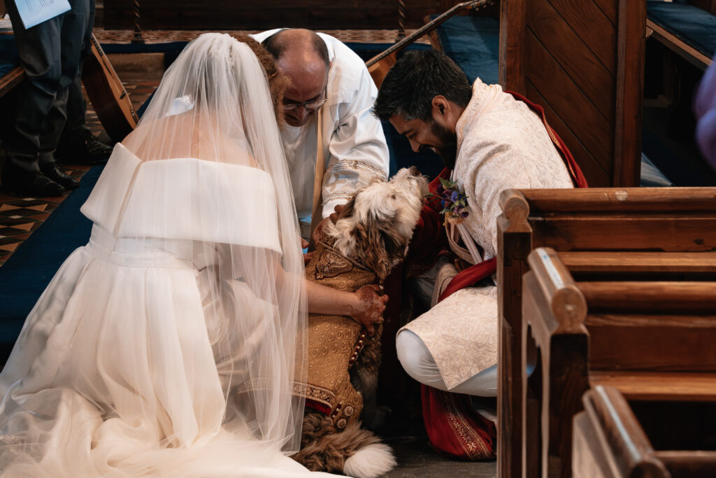 A bride, groom and vicar are kneeling at the front of the alter to collect rings from a dog ring bearer